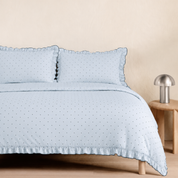 Elsie Spot Bedding Set in Cloud Blue, made bed with gathered frill edges beside a wooden side table