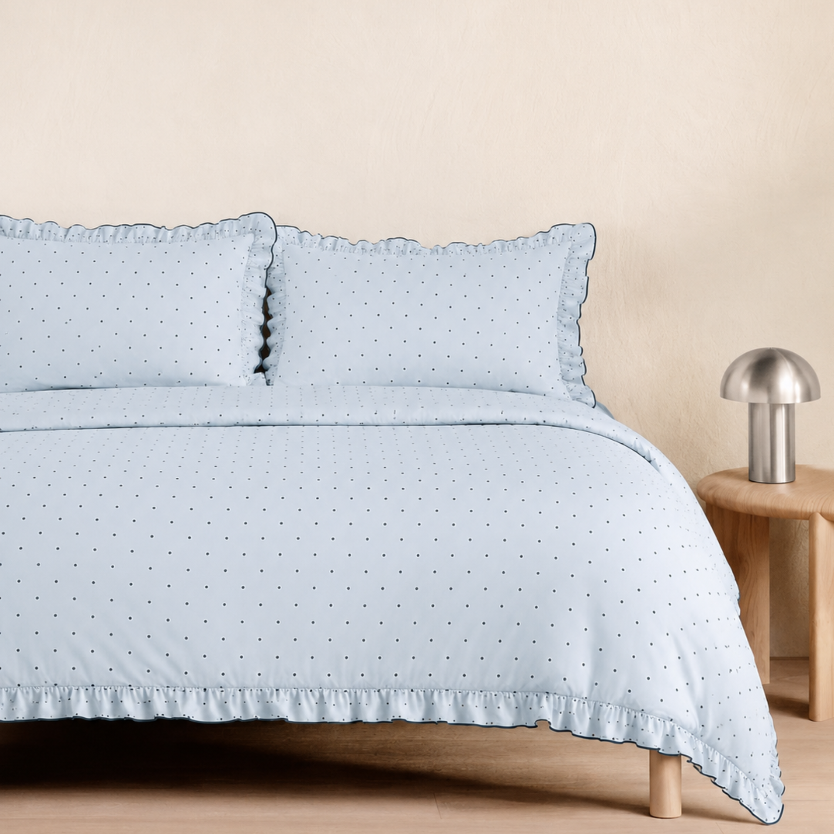 Elsie Spot Bedding Set in Cloud Blue, made bed with gathered frill edges beside a wooden side table