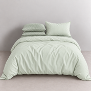 Honeythatch Gingham Bedding Set in Sage, styled on a bed with striped and check pillowcases layered