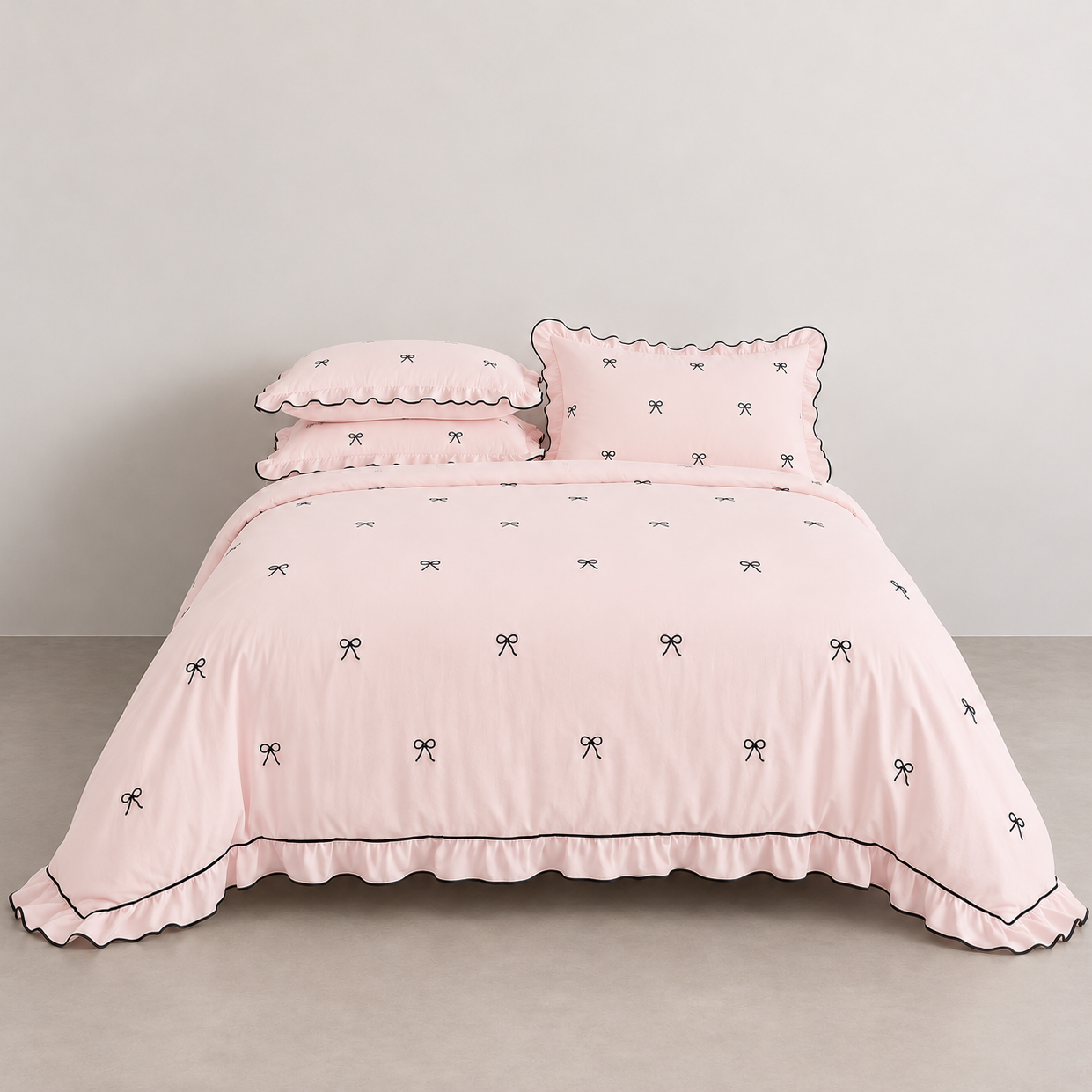 Isabella Bow Bedding Set in Blush, made bed with scalloped edges and embroidered bow print, black piping trim