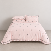Isabella Bow Bedding Set in Blush, made bed with scalloped edges and embroidered bow print, black piping trim