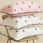 Isabella Bow Bedding Set pillowcases stacked in blush and ivory with black bow embroidery and wavy trim