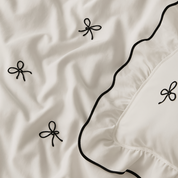 Close-up of the Isabella Bow Bedding Set in Ivory, showing bow embroidery and black piped edge on twill