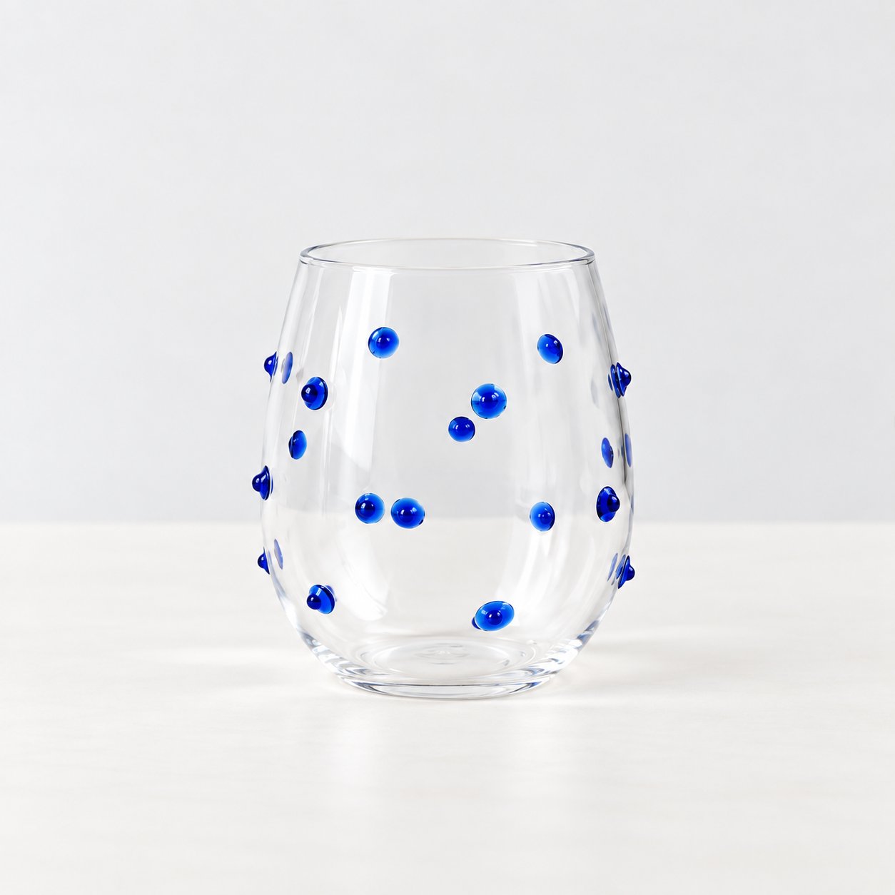 Isla Freckle Glass Tumbler in Blue, clear stemless glass dotted with raised cobalt beads, on a plain surface