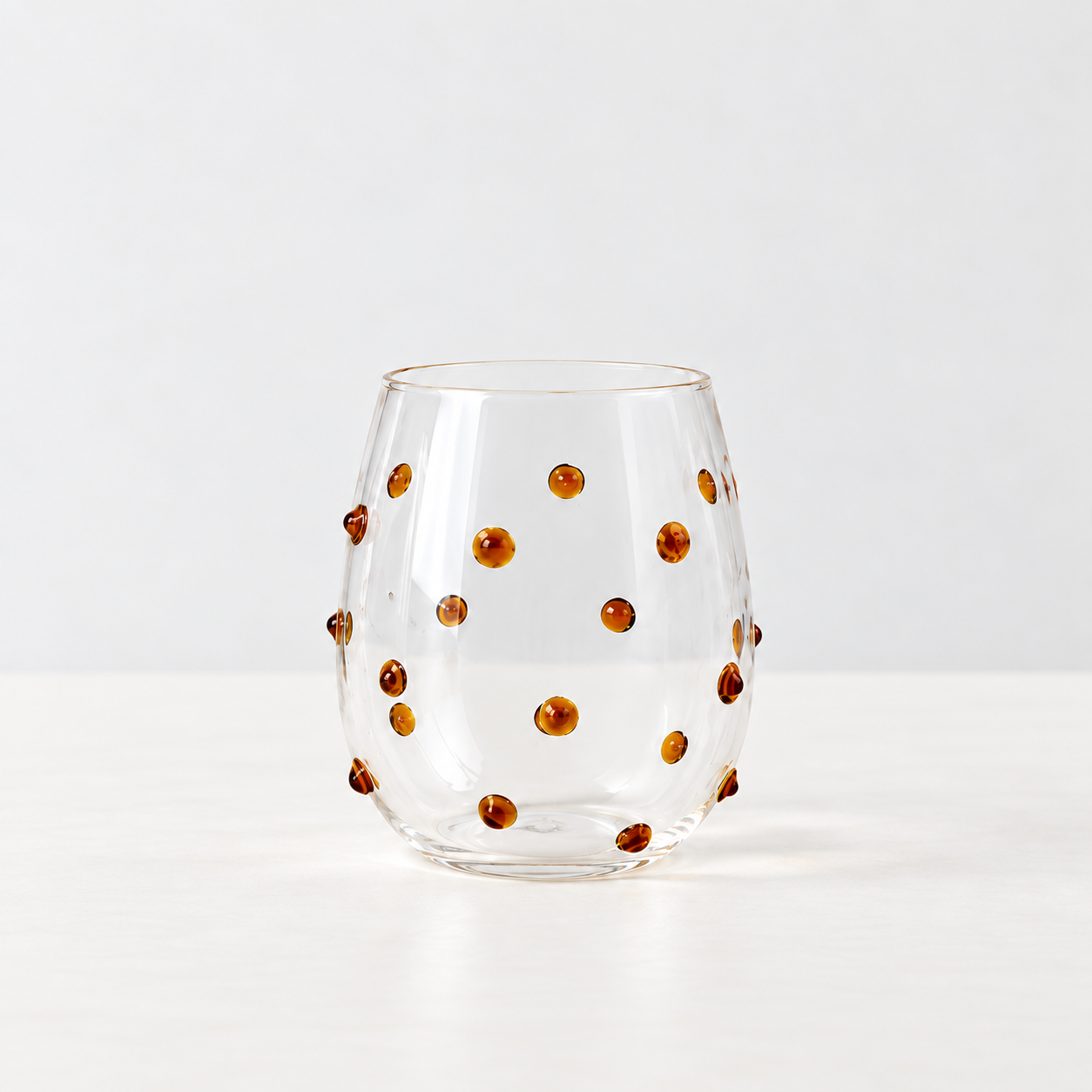 Isla Freckle Glass Tumbler in Yellow, clear stemless glass with raised amber dots scattered across the surface