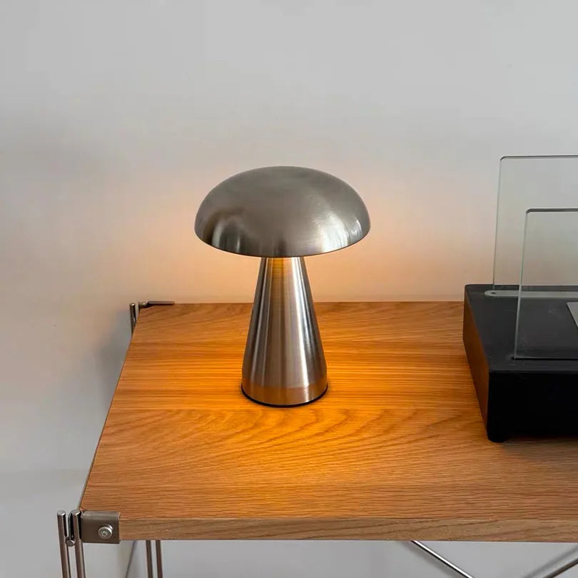 Jaz Chrome Desk Lamp in Silver, dome head glowing warm light on a wooden table beside a glass frame
