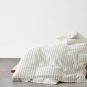 Juno Stripe Bedding Set in cream with charcoal stripes, cotton draped over a timber bed frame edge