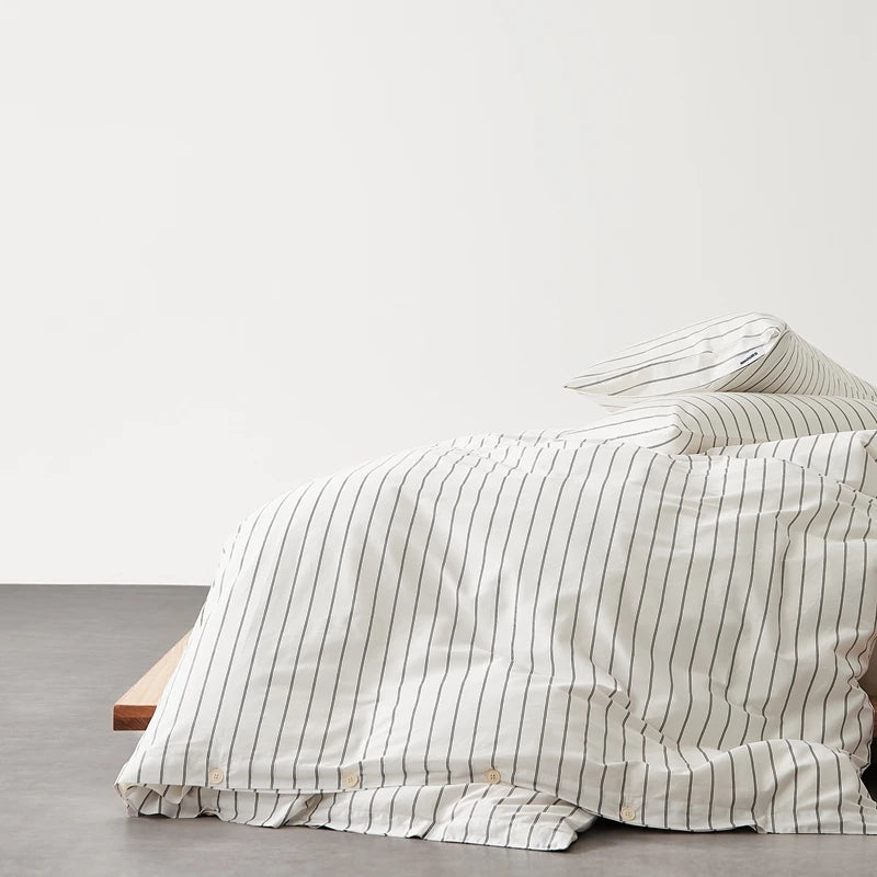 Juno Stripe Bedding Set in cream with charcoal stripes, cotton draped over a timber bed frame edge