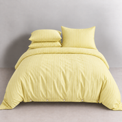 Juno Stripe Bedding Set in Soleil, a made bed with buttoned quilt cover and stacked pillowcases in soft yellow