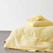 Juno Stripe Bedding Set in Soleil, sunny yellow cotton with subtle stripe, button-cornered quilt cover on a low bed