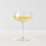 Lennon Pearl Coupe Glass with beaded studs on the bowl, filled with sparkling wine on a table