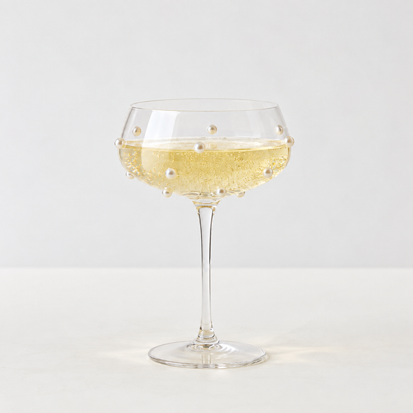 Lennon Pearl Coupe Glass with beaded studs on the bowl, filled with sparkling wine on a table