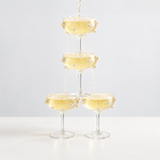 Four Lennon Pearl Coupe Glasses stacked in a tower, champagne cascading over pearl beading between tiers