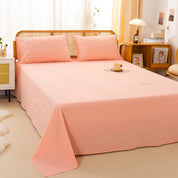 Luna Cotton Flat Sheet in Apricot Sorbet, styled on a rattan bed with matching pillowcases