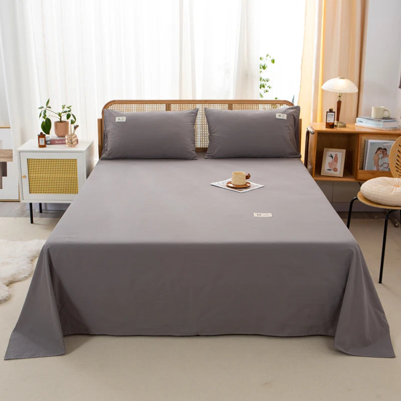 Luna Cotton Flat Sheet in Cool Stone grey, styled on a rattan bed with matching pillowcases