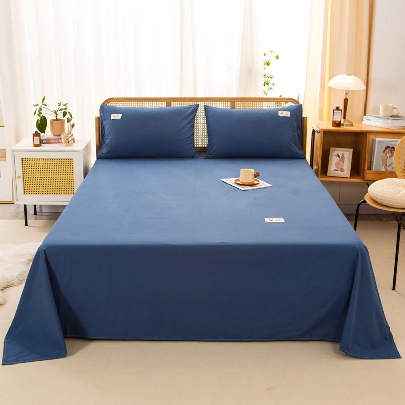 Luna Cotton Flat Sheet in Midnight Coast, deep blue, dressed on a bed with matching pillowcases in a rattan bedroom