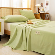 Luna Cotton Flat Sheet in Sage Pear, draped over a rattan bed with pillowcases and a bedside tray