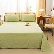 Luna Cotton Flat Sheet in Sage Pear dresses a rattan bed beside a cane chair and warm lamplight