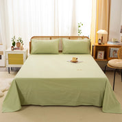 Luna Cotton Flat Sheet in Sage Pear, sage green, draped over a bed with matching pillowcases in a bright room
