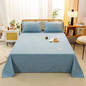 Luna Cotton Flat Sheet in Sky Mist, dressed over a rattan bed with pillowcases, book and mug styled on top