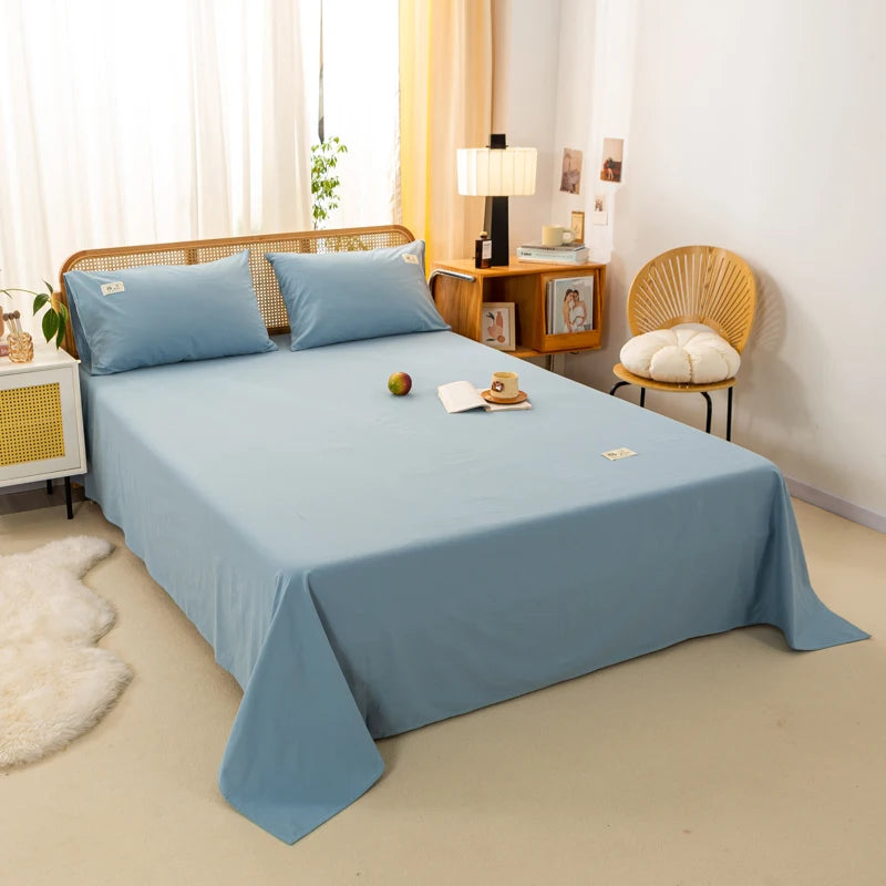 Luna Cotton Flat Sheet in dusty blue, styled on a rattan bed with matching pillowcases and a book tray
