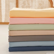 Luna Cotton Flat Sheet folded stack in yellow, apricot, sage, oat, grey, blue and navy tones
