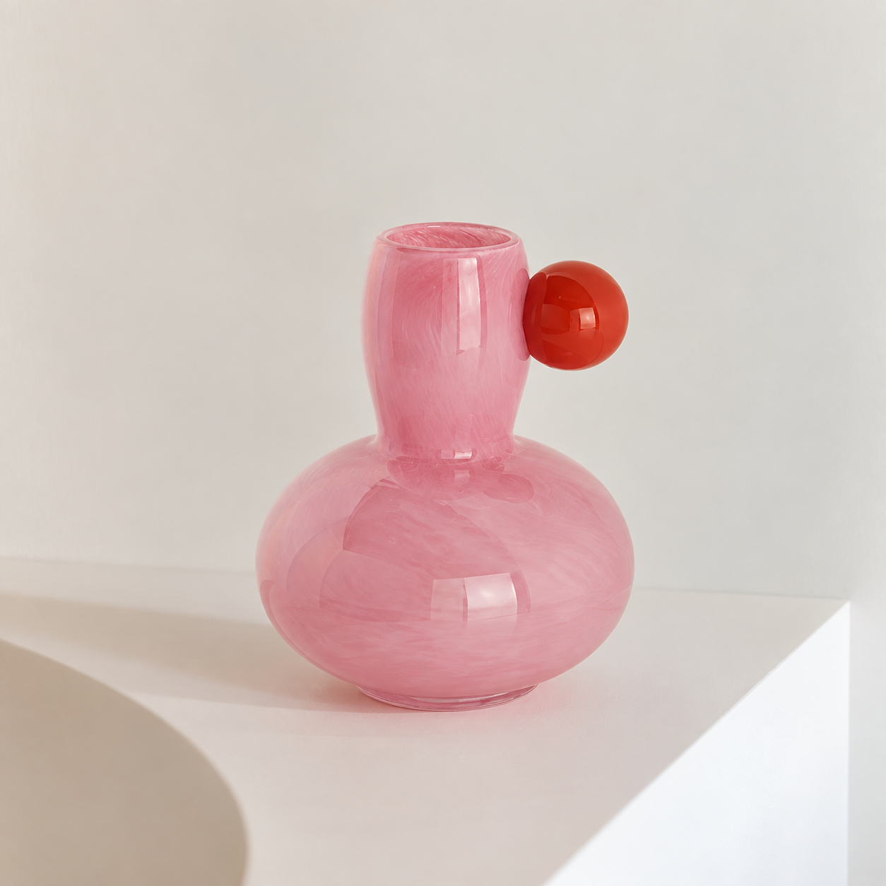 Marley Pastel Vase in Pink, gourd shaped glass body with a red sphere accent at the neck, on a white ledge