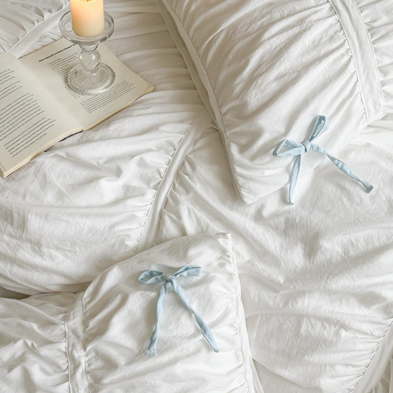 Metaya Bedding Set in Blue & White, ruched white cotton with pale blue ties, styled with a book and candle