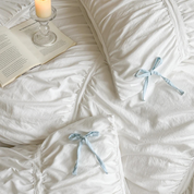 Metaya Bedding Set in Blue & White, ruched white cotton with pale blue ties, styled with a book and candle