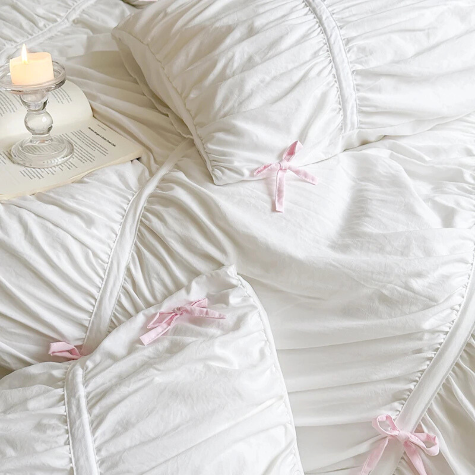 Metaya Bedding Set in white with ruched texture and pink ribbon ties, styled with a candle and open book
