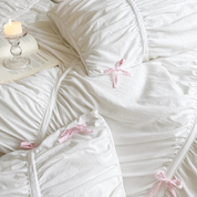 Metaya Bedding Set in white with ruched texture and pink ribbon ties, styled with a candle and open book