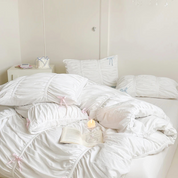 Metaya Bedding Set in white with ruched pillowcases, pink and blue ribbon ties, styled with a candle and book