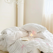 Metaya Bedding Set rumpled in white with pink bow ties, candle and open book styled on the bed