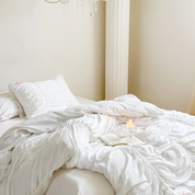 Metaya Bedding Set in soft white, ruched quilt cover rumpled on a bed with candle and open book