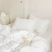 Metaya Bedding Set in white with ruched texture, styled bed with pink tie detail, candle and book