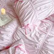 Metaya Bedding Set in blush pink with ruched texture and ribbon ties, styled with a candle and open book