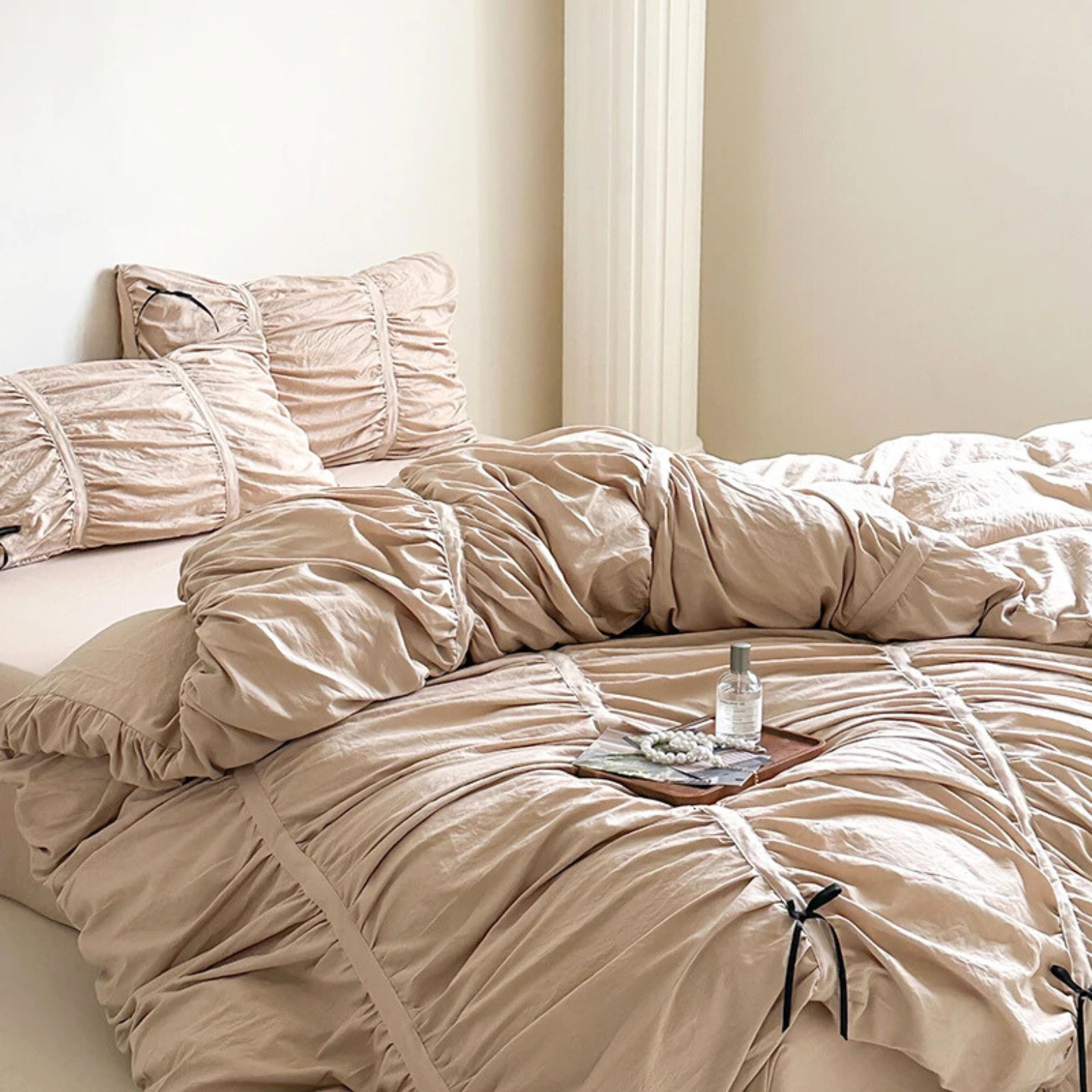 Metaya Bedding Set in beige twill cotton, ruched with tie details, styled on a bed with a small tray