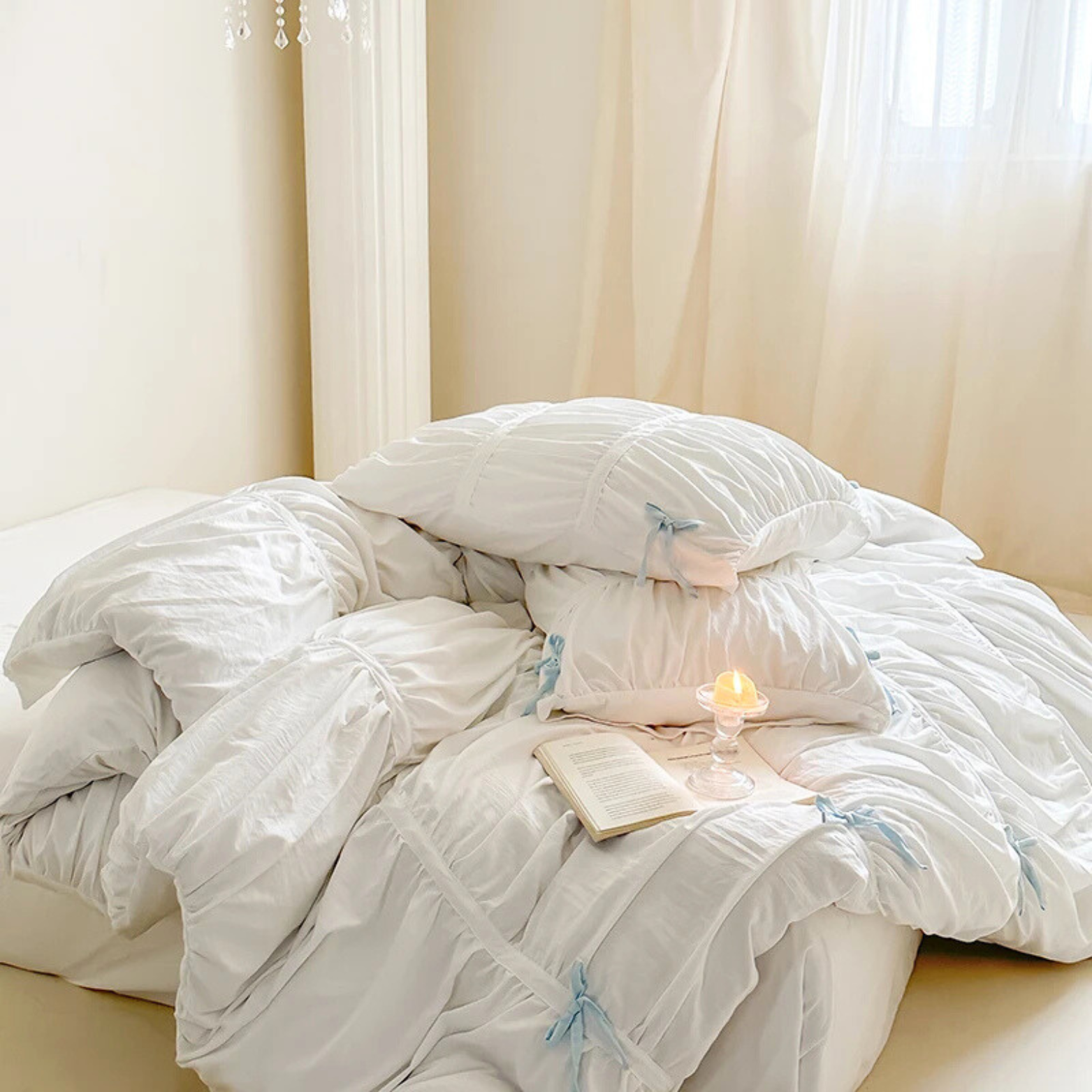 Metaya Bedding Set in white with pale blue ribbon ties, ruched pillows styled with a candle and book