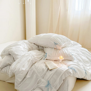 Metaya Bedding Set in white with pale blue ribbon ties, ruched pillows styled with a candle and book