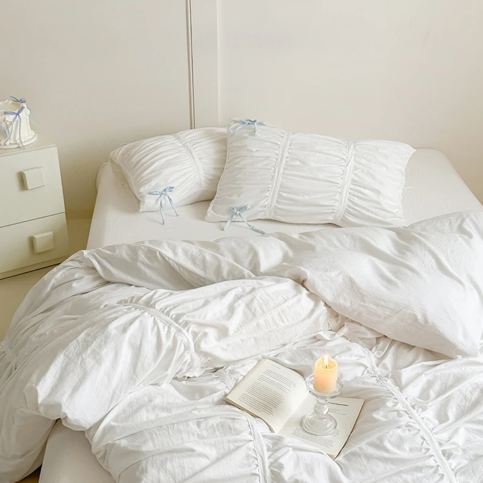 Metaya Bedding Set in white with ruched pillowcases and pale blue ties, styled with a candle and book