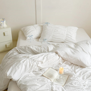 Metaya Bedding Set in white with ruched pillowcases and pale blue ties, styled with a candle and book