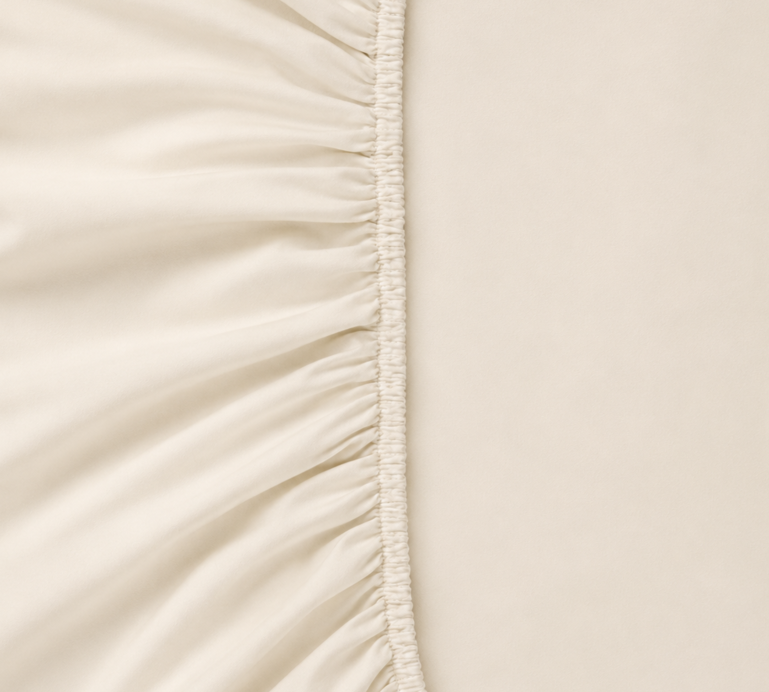 Close-up of the Mira Bamboo Fitted Sheet's gathered elastic edge in soft cream, showing the silky weave
