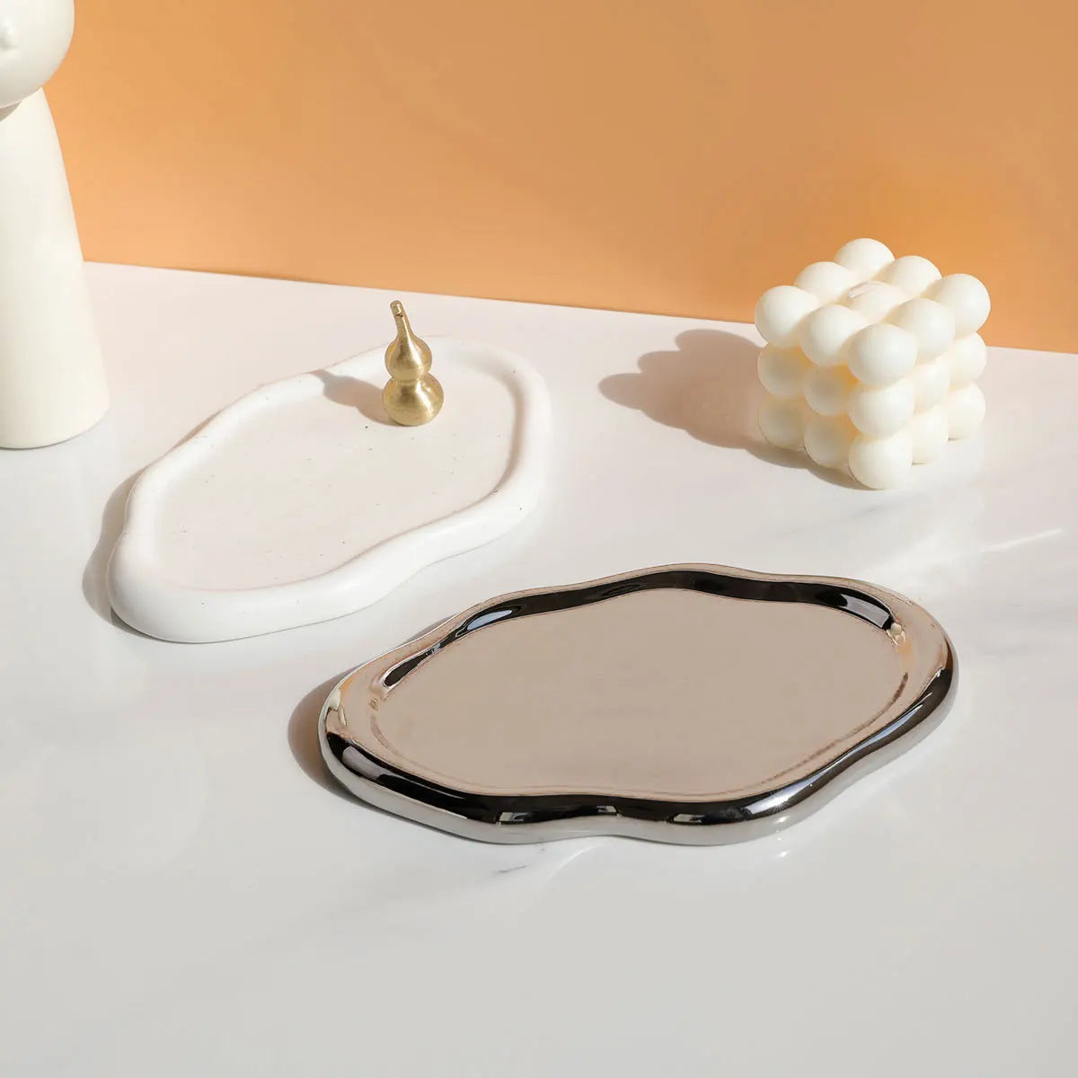 Nola Trinket Tray shown with a chrome-rimmed cloud shape beside a matte white version and small props