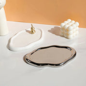 Nola Trinket Tray shown with a chrome-rimmed cloud shape beside a matte white version and small props