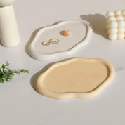 Nola Trinket Tray in cloud-like ivory and pale yellow, one holding earrings and a stone bead