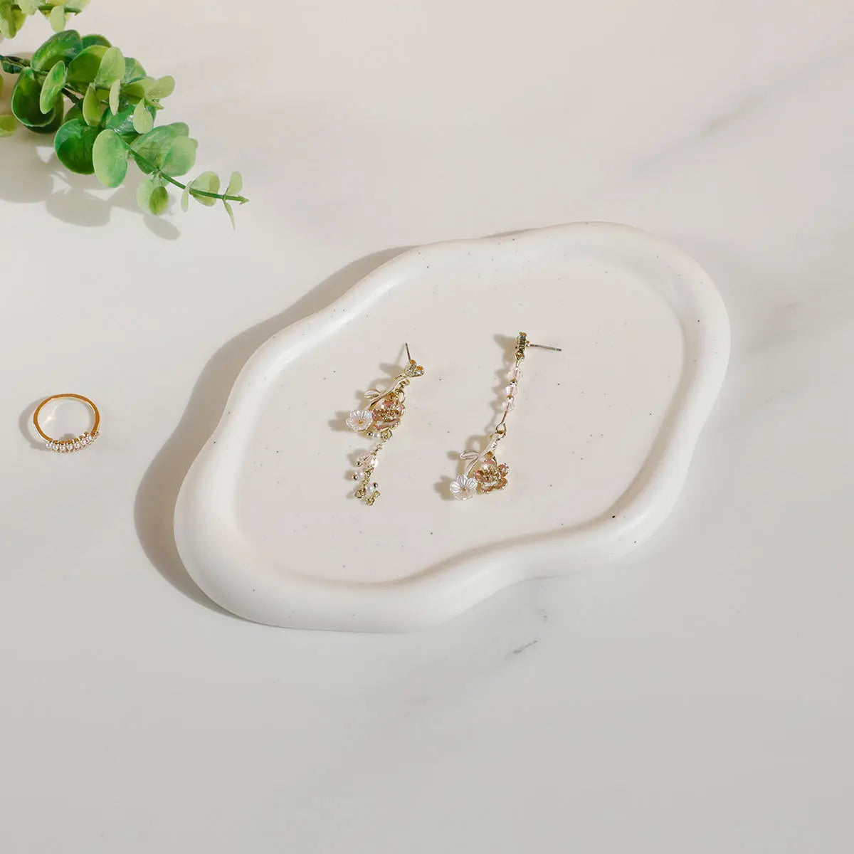 Nola Trinket Tray in cloud-shaped cream ceramic, holding drop earrings beside a ring and greenery
