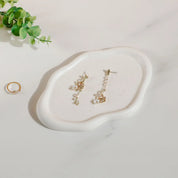 Nola Trinket Tray in cloud-shaped cream ceramic, holding drop earrings beside a ring and greenery