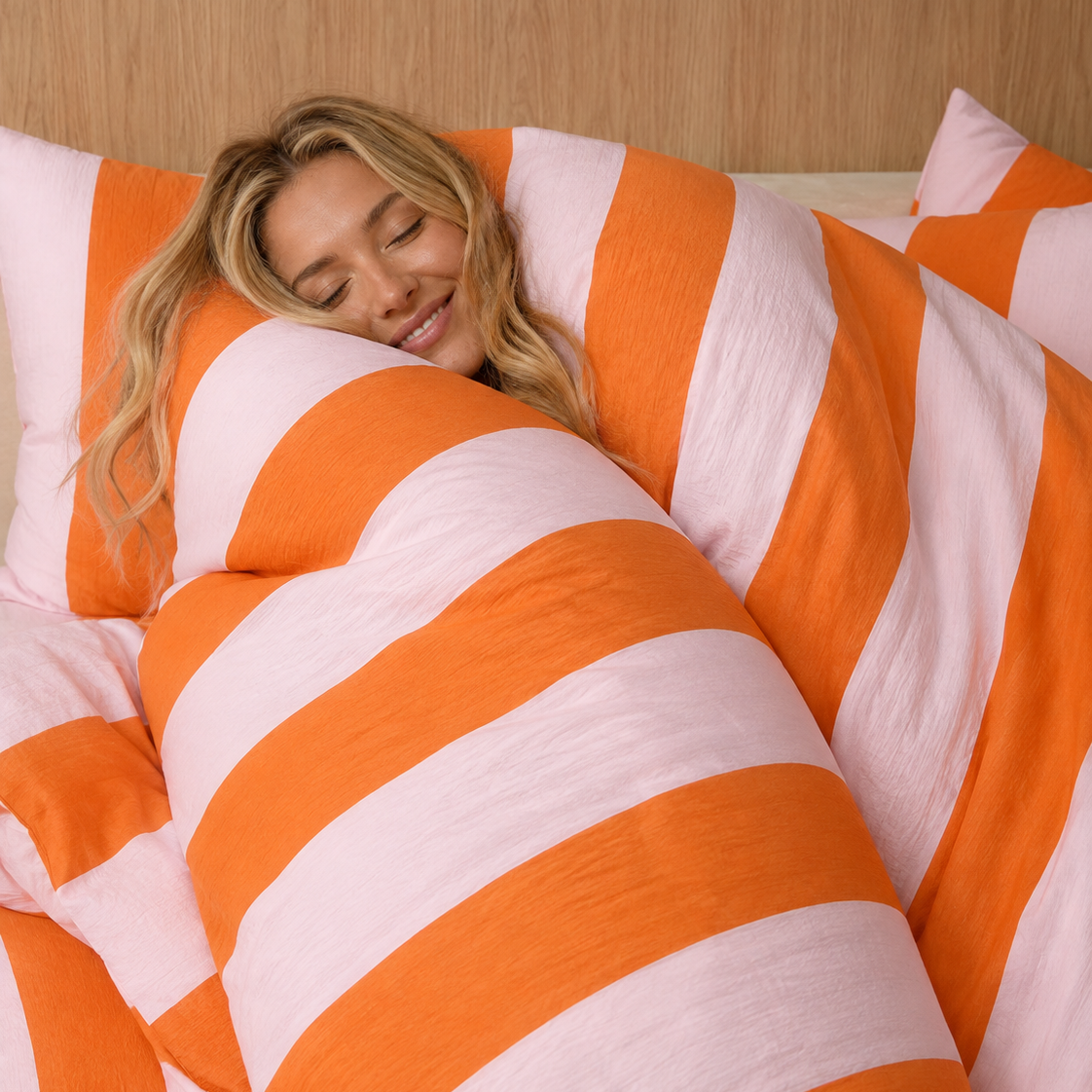Woman resting among wide grapefruit pink and orange stripes of the Ravello Stripe Bedding Set