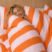 Woman resting among wide grapefruit pink and orange stripes of the Ravello Stripe Bedding Set