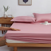 Hands fit the elasticated edge of the Sola Cotton Fitted Sheet in Blush pink onto a wooden bed frame